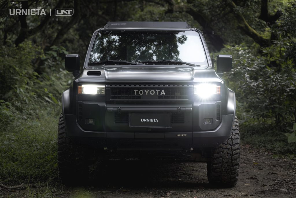 URNIETA LC250 Front Fascia Kit on a Toyota Land Cruiser 250, head-on view with headlights on, parked on a dark forest trail