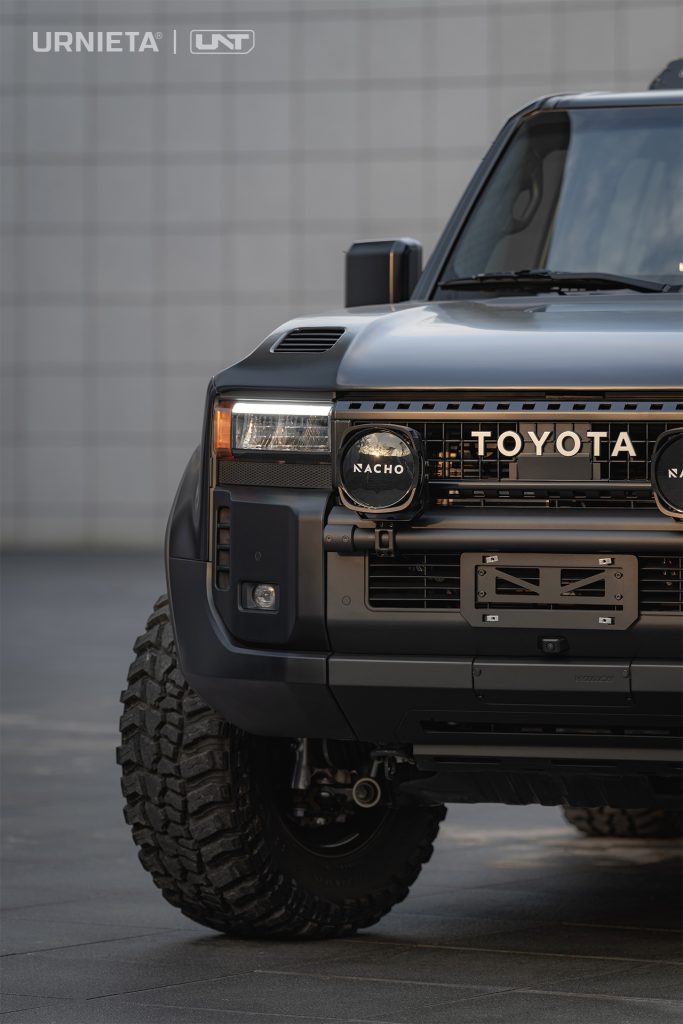 URNIETA LC250 Front Fascia Kit on a Toyota Land Cruiser 250, front corner close-up with two round auxiliary lights on the mini bull bar, tiled wall behind
