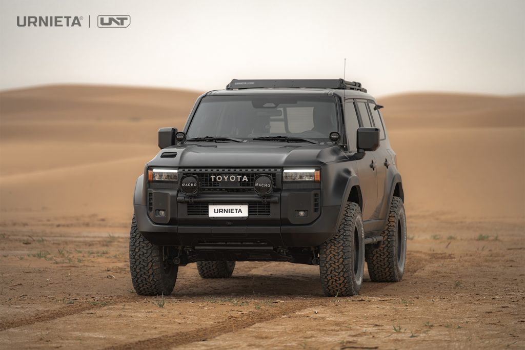 URNIETA LC250 Front Fascia Kit on a Toyota Land Cruiser 250, head-on view parked in sand dunes with auxiliary lights