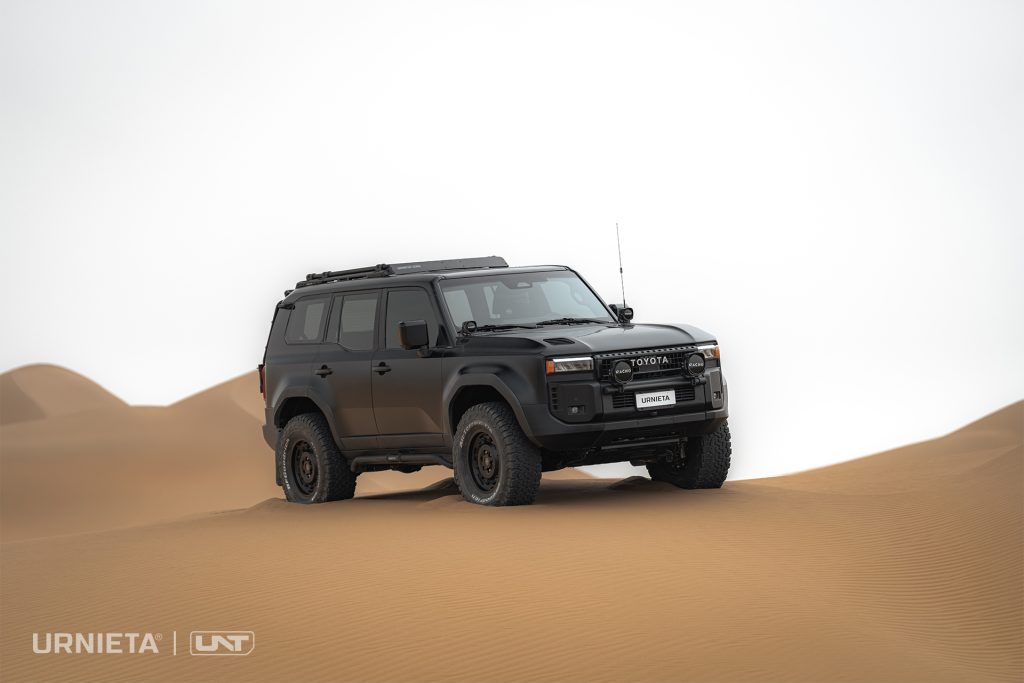 URNIETA LC250 Front Fascia Kit on a Toyota Land Cruiser 250, front three-quarter view on a dune crest against a bright sky